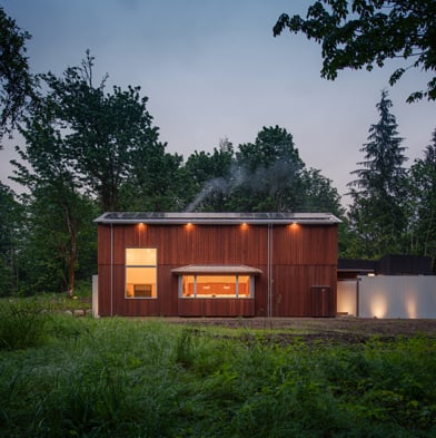 A home surrounded by woods and mountains with vertical cedar cladding and a large bay window.